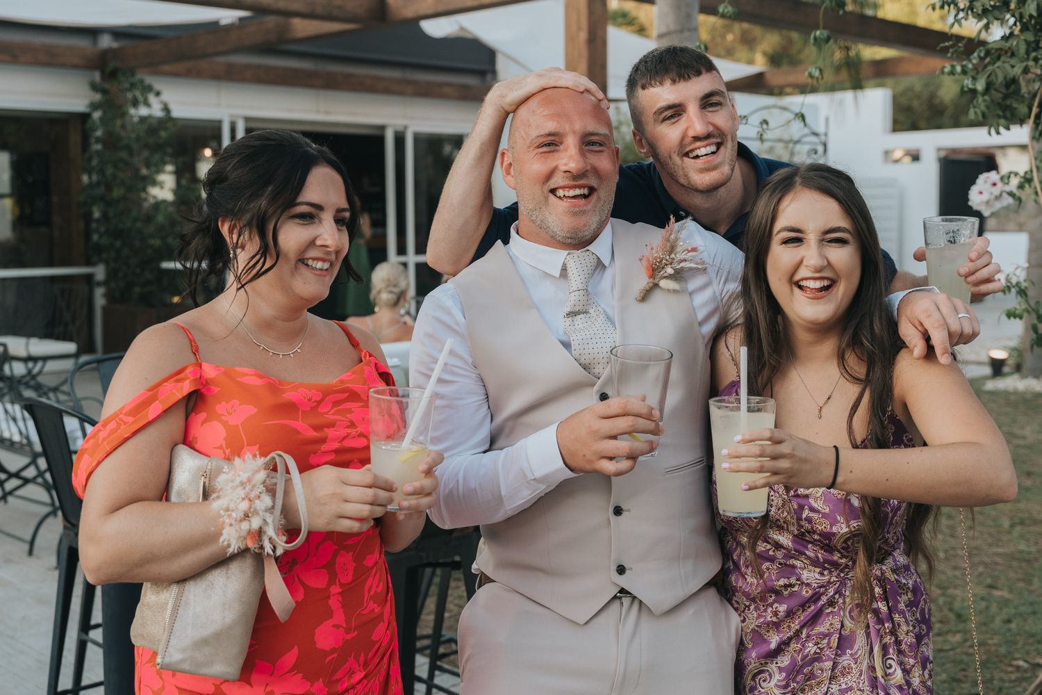 Group of people at an outdoor celebration enjoying drinks and smiling while dressed in formal attire.