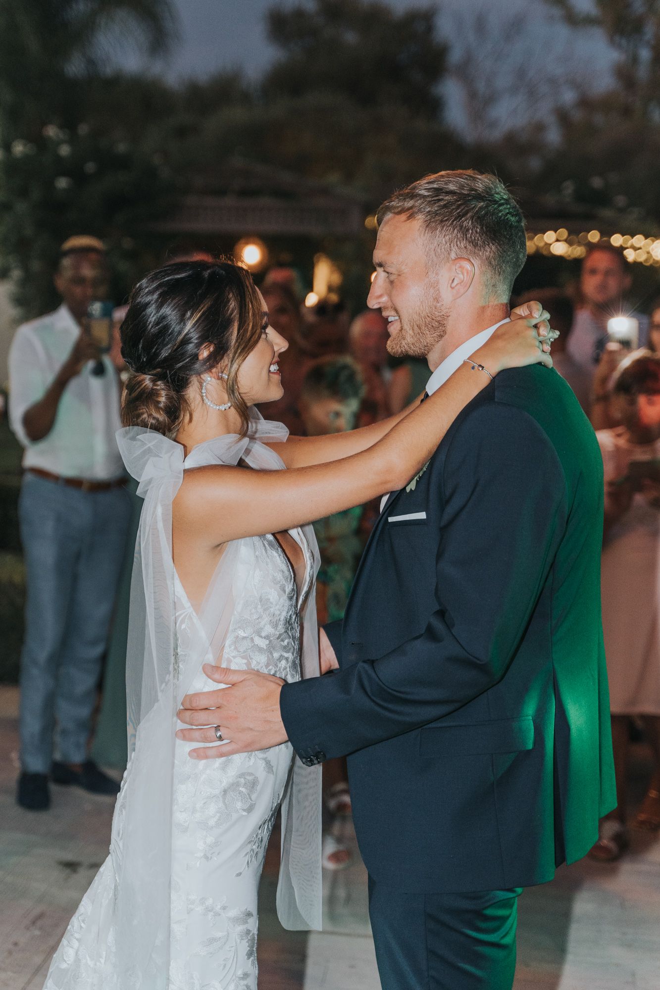 A romantic moment between newlyweds dancing under evening lights at their outdoor reception.