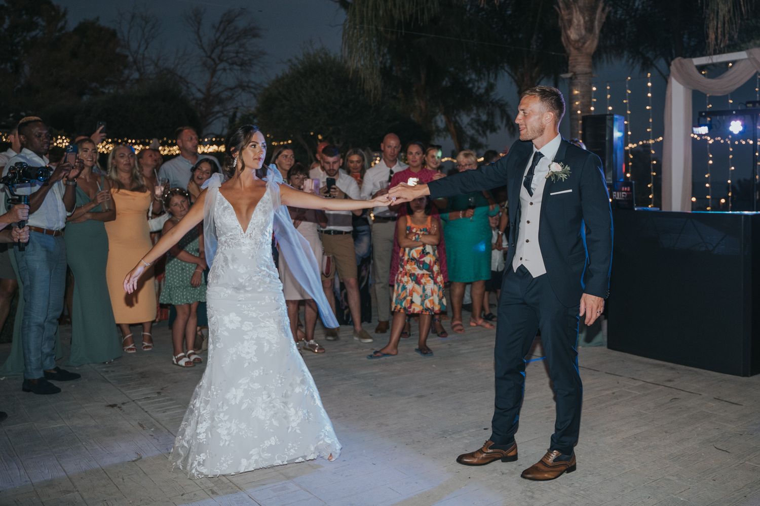 A couple performs their first dance on an outdoor dance floor at a wedding reception as guests watch and celebrate.