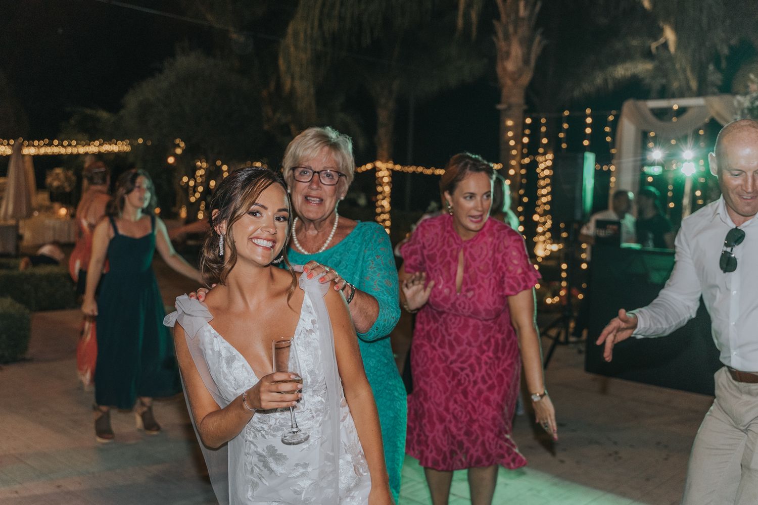 Wedding guests dancing and celebrating at an outdoor evening reception with string lights.