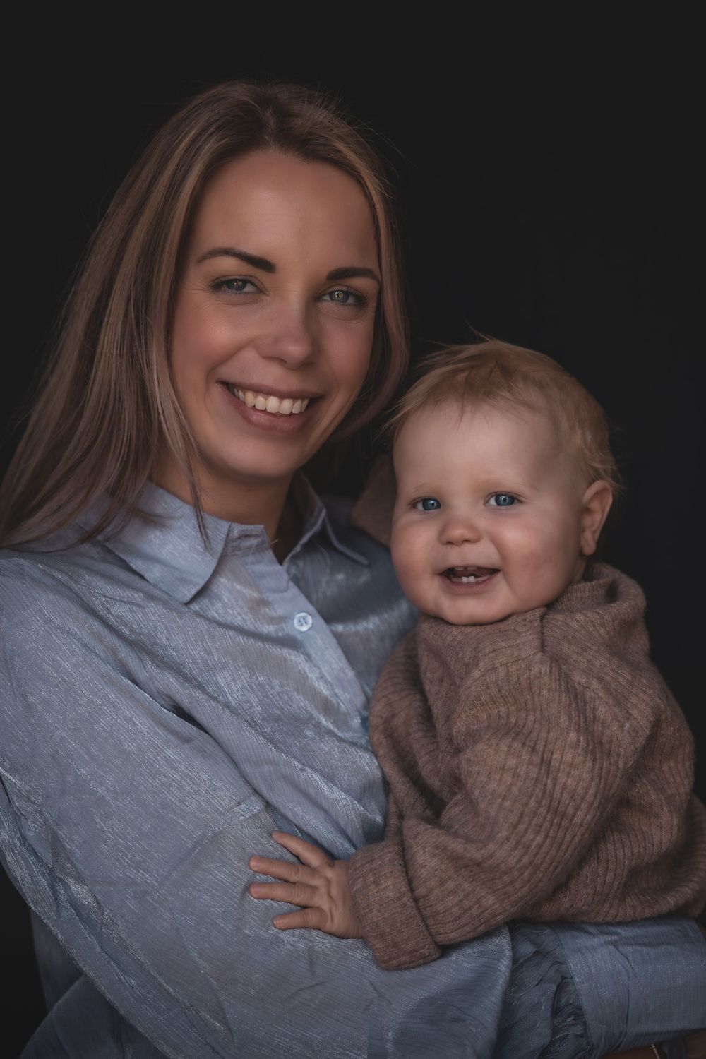 A heartwarming studio portrait featuring warm smiles and embraces against a dark background.