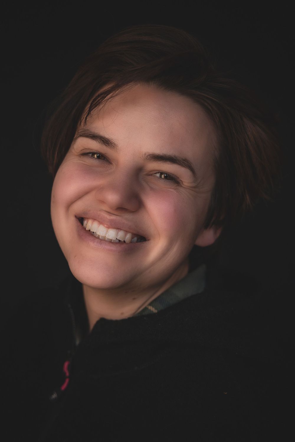 Portrait photo showing bright smile and warm expression against dark background.