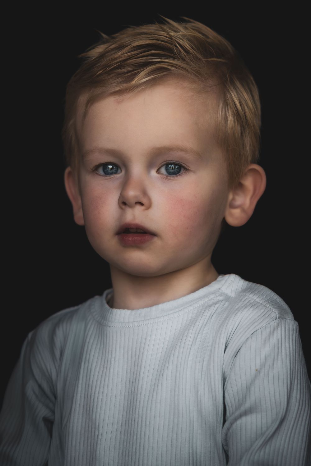 A series of dramatic black and white portraits showing a child in a white ribbed sweater against a dark background.