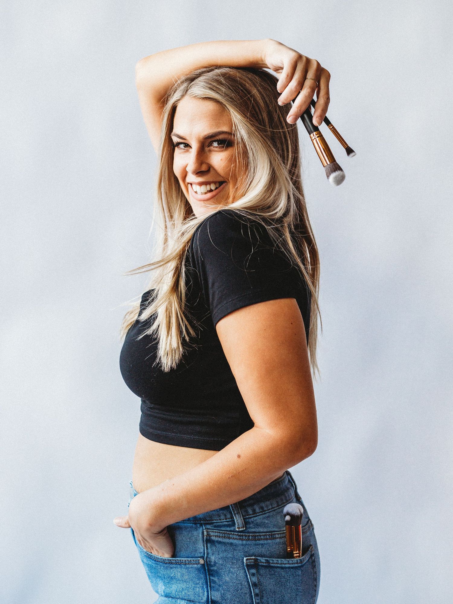 Woman in black crop top and jeans posing with tools against white background.