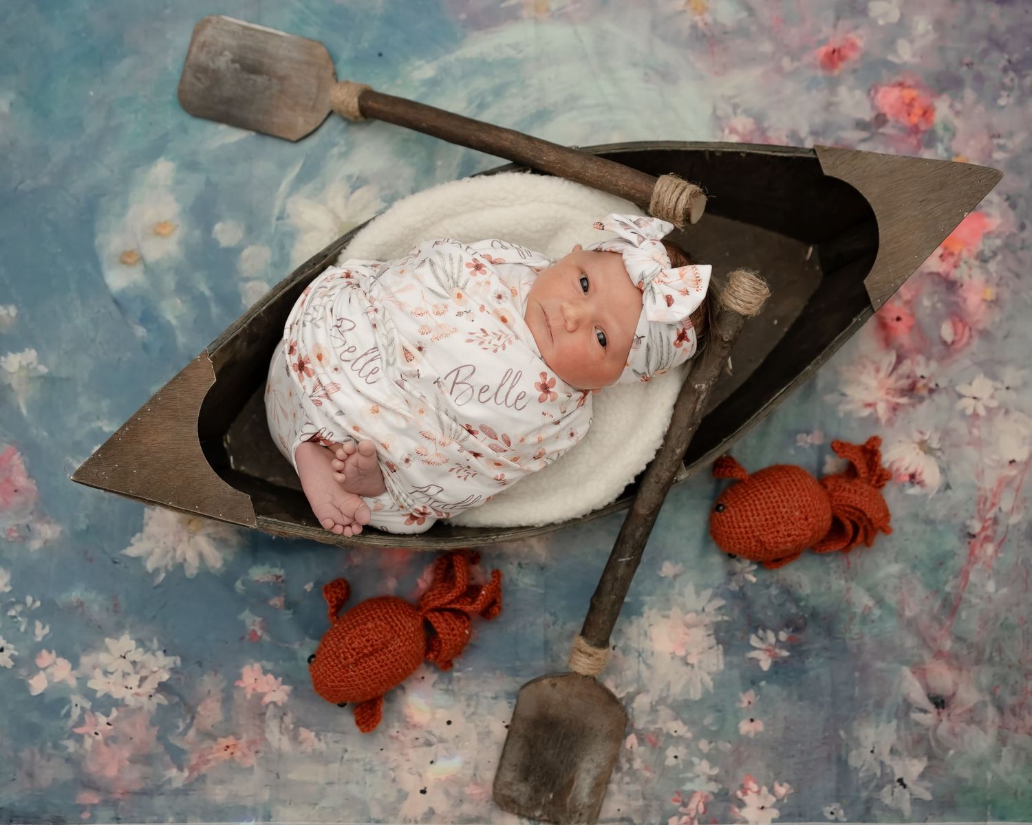 Baby bundled in white blanket lying in vintage metal coal shovel with red knit accessories on artistic backdrop.