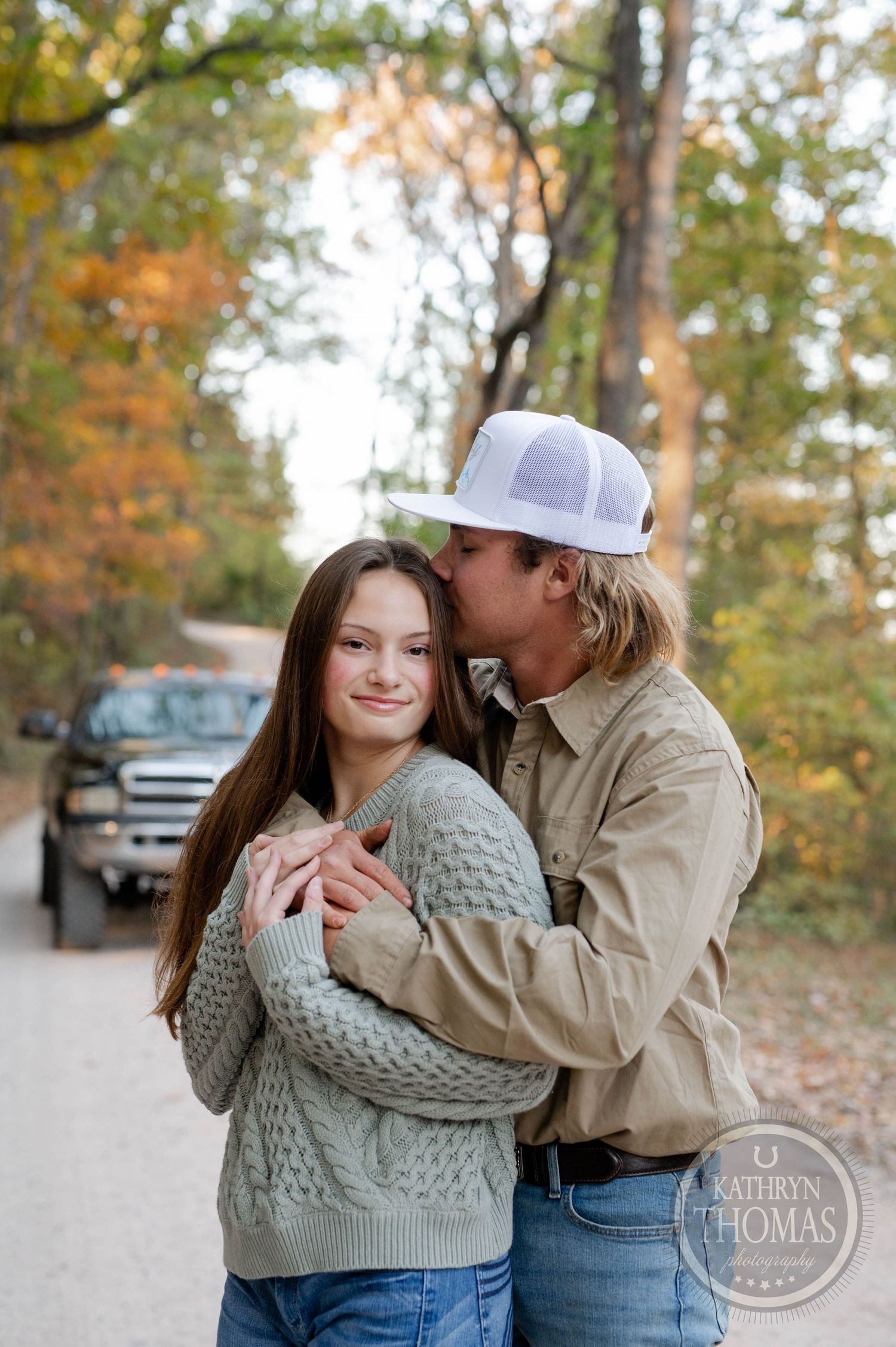 A tender moment between a couple wearing cozy sweaters on a forest path in fall.