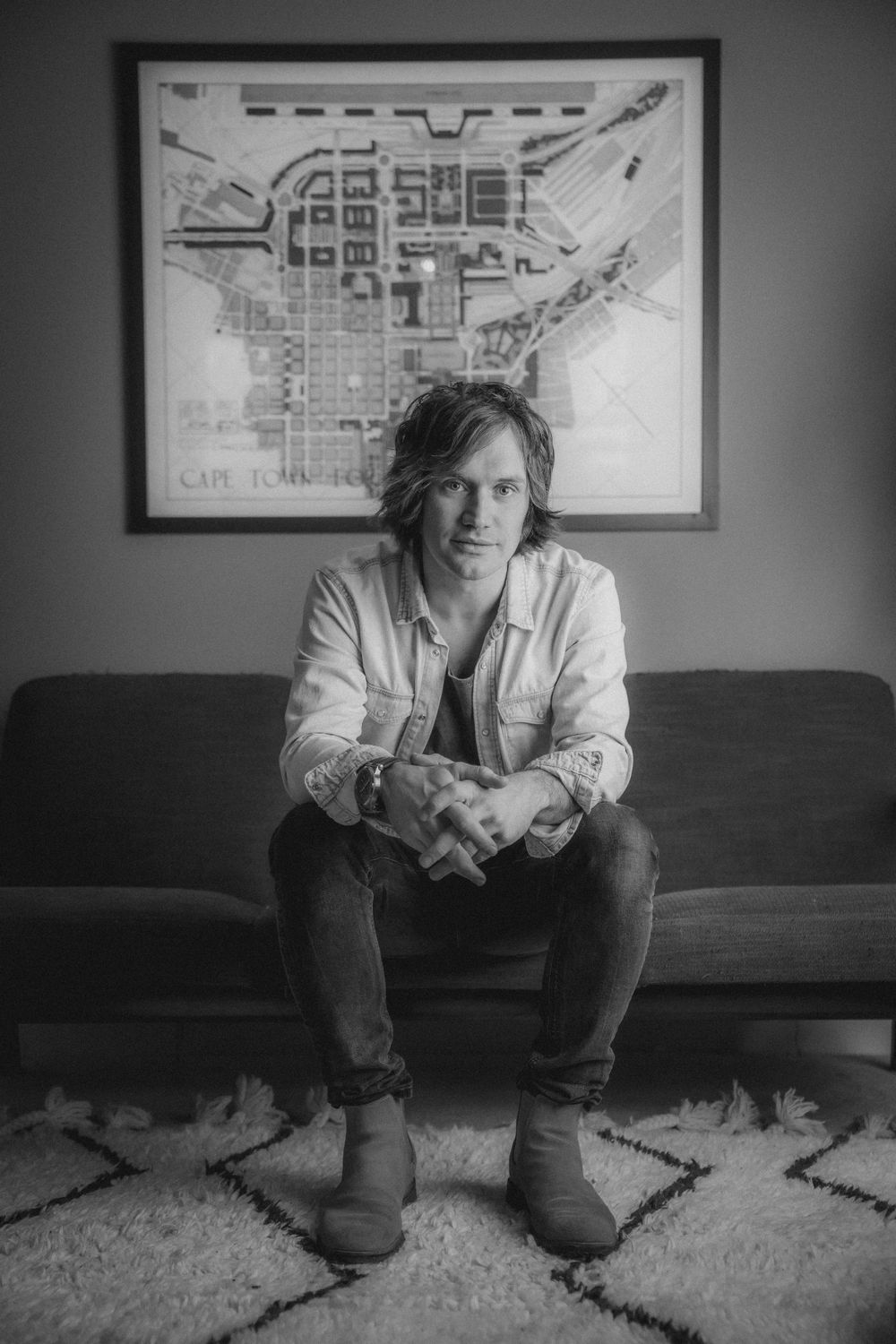 Person sits on couch beneath framed city map in monochrome portrait.