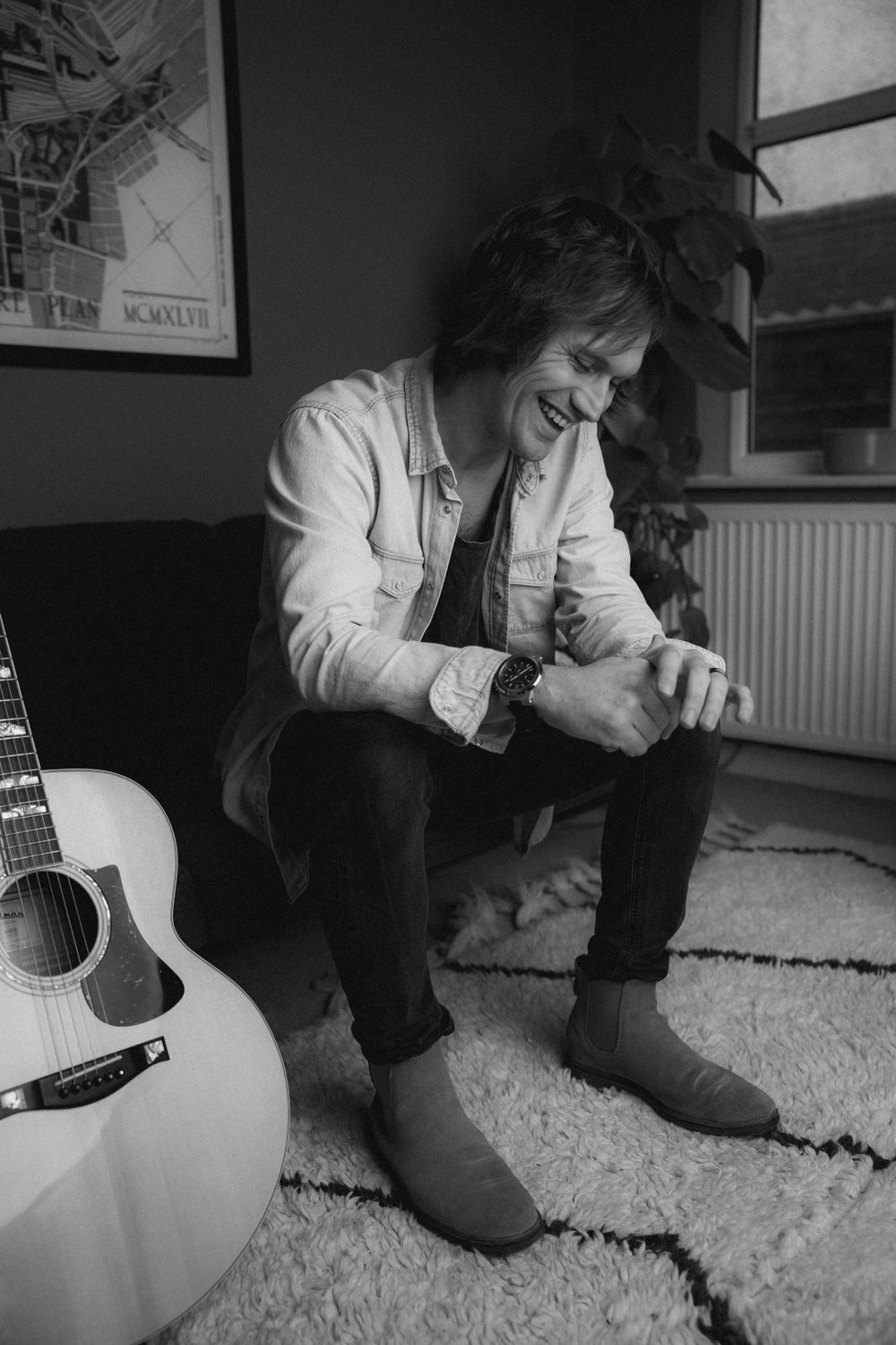 Casual portrait of person laughing on couch with acoustic guitar nearby.