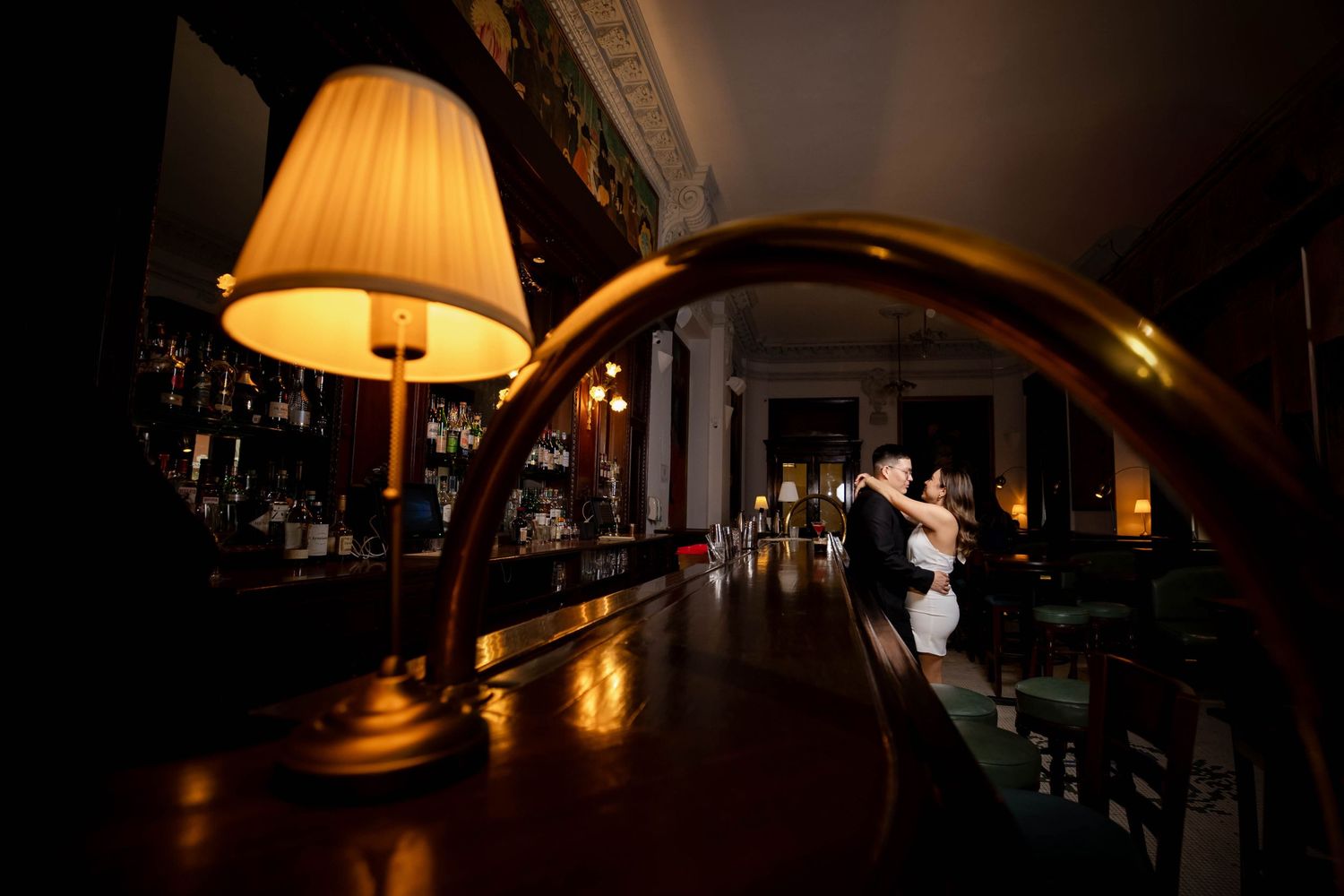 Two silhouetted dancers embrace on a darkened dance floor illuminated by warm lamp light and reflective bar surfaces.