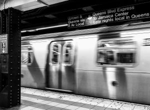 A blurred motion shot of a New York City subway train passing through a station in black and white.