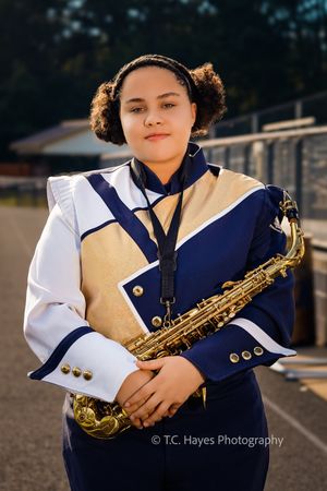 Marching band member poses in navy and white uniform while holding a saxophone on a sunny afternoon.