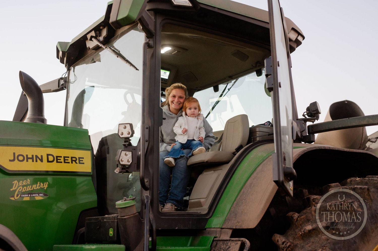 A John Deere tractor cabin with occupants looking out over farmland during daytime.