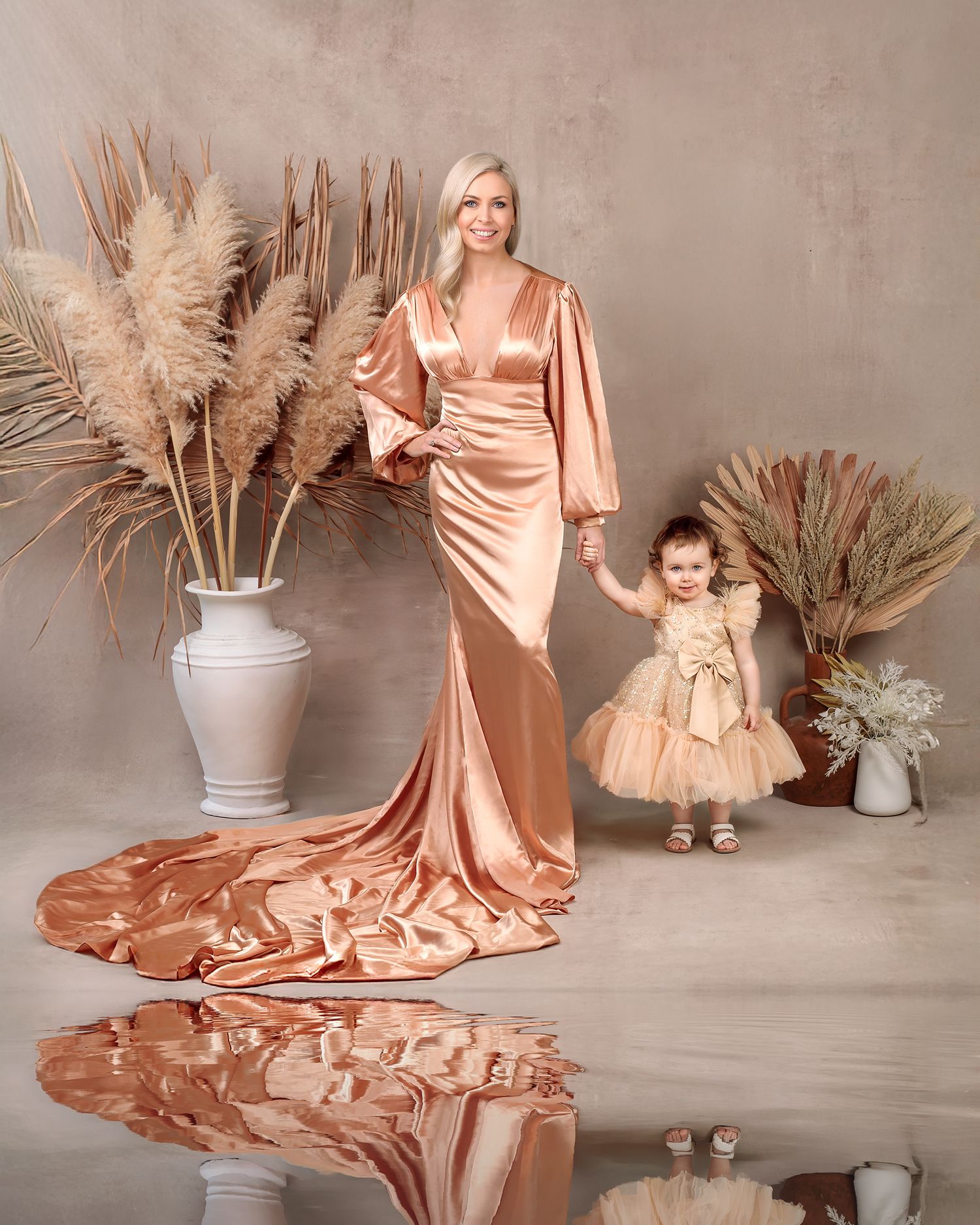 Mum and daughter wearing matching dresses, both smiling holding hands in a luxury scene.