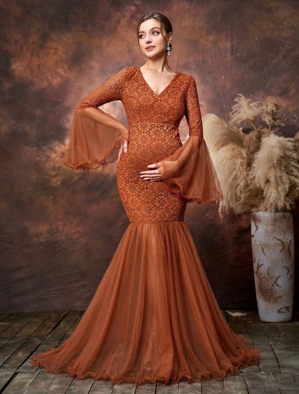 Maternity portraits in rust-colored lace gown against brown backdrop with pampas grass accents.