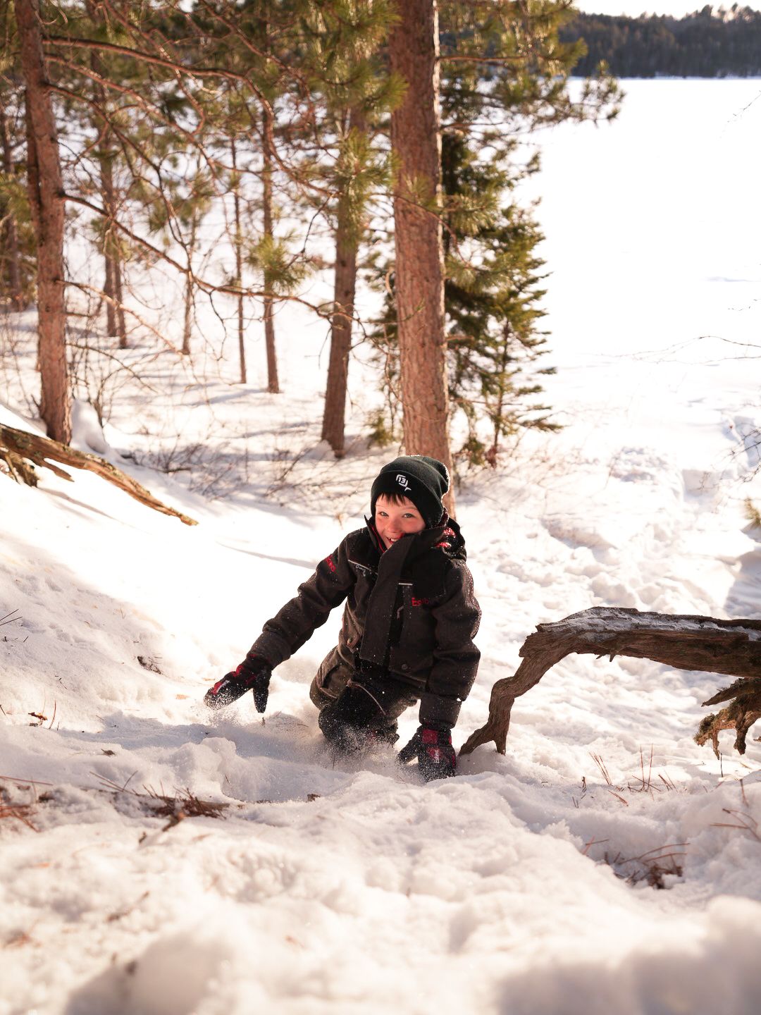 Winter adventurer playing in deep snow among pine trees near frozen lake.
