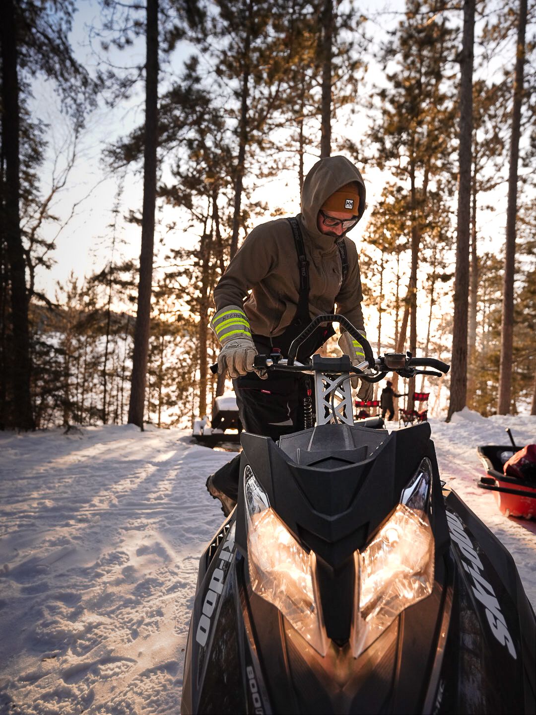Snowmobile rider navigating through snowy forest trails at golden hour.