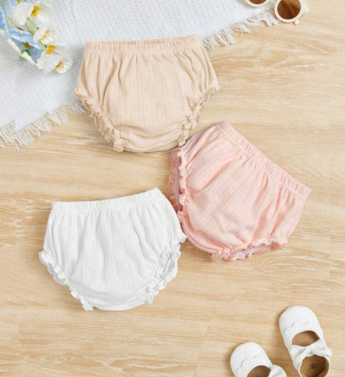 Soft pastel baby bloomers in white, pink and peach displayed on wooden surface.