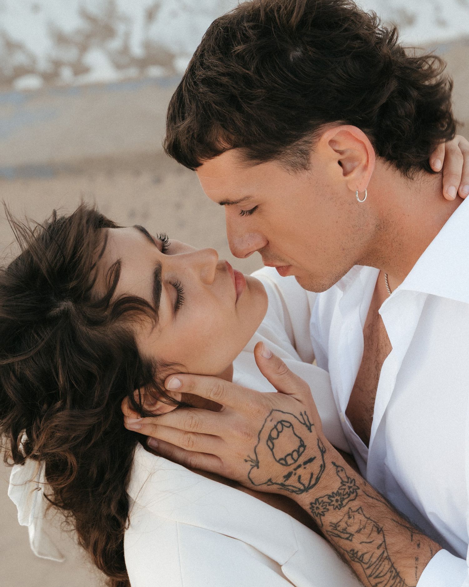 An intimate romantic moment between a couple on a beach, with arms wrapped tenderly around each other.