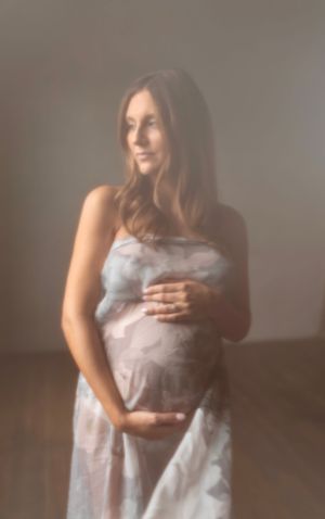 Ethereal maternity portrait of woman in flowing white dress against soft focus background.