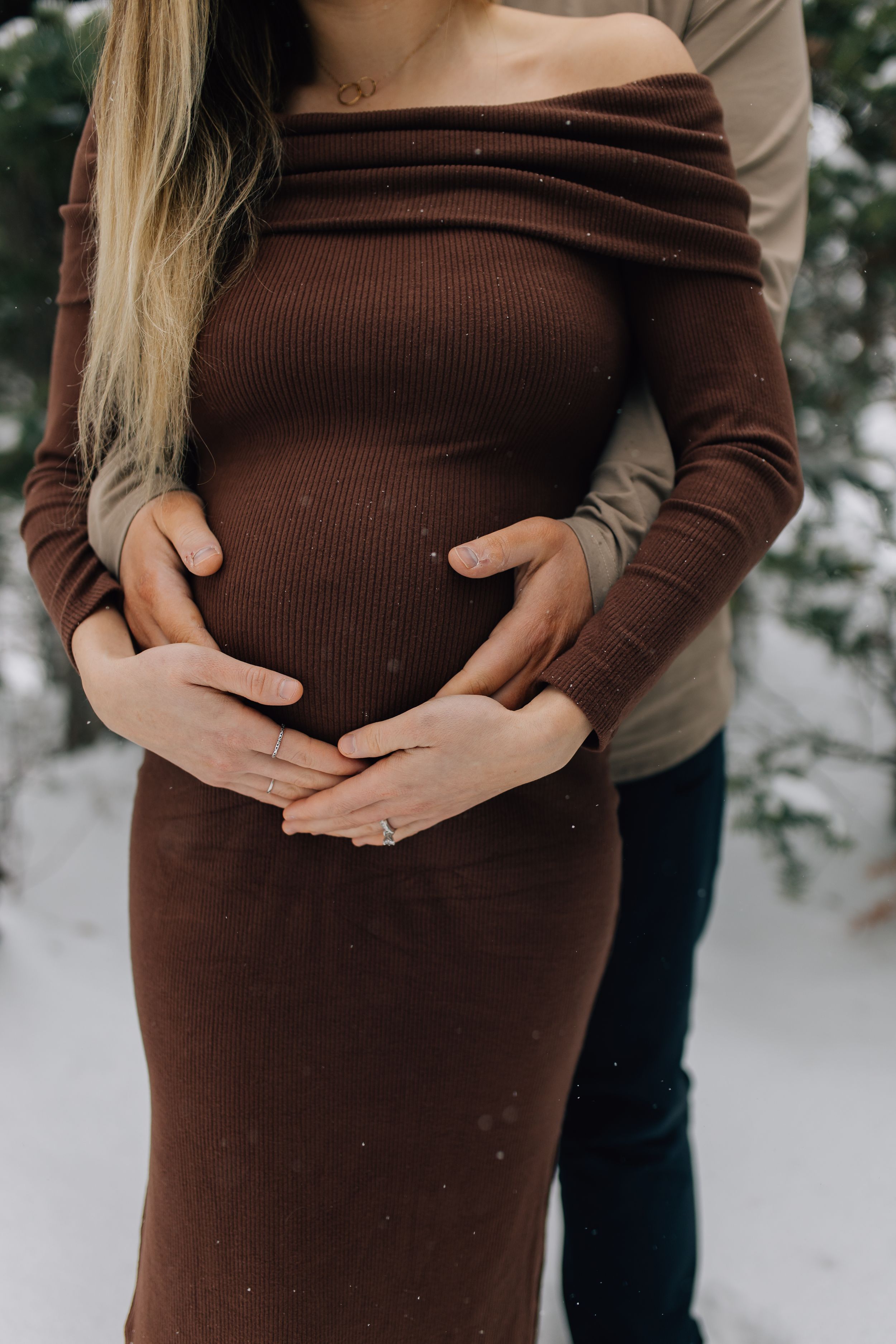 Maternity photo showing hands cradling pregnant belly in brown sweater dress.