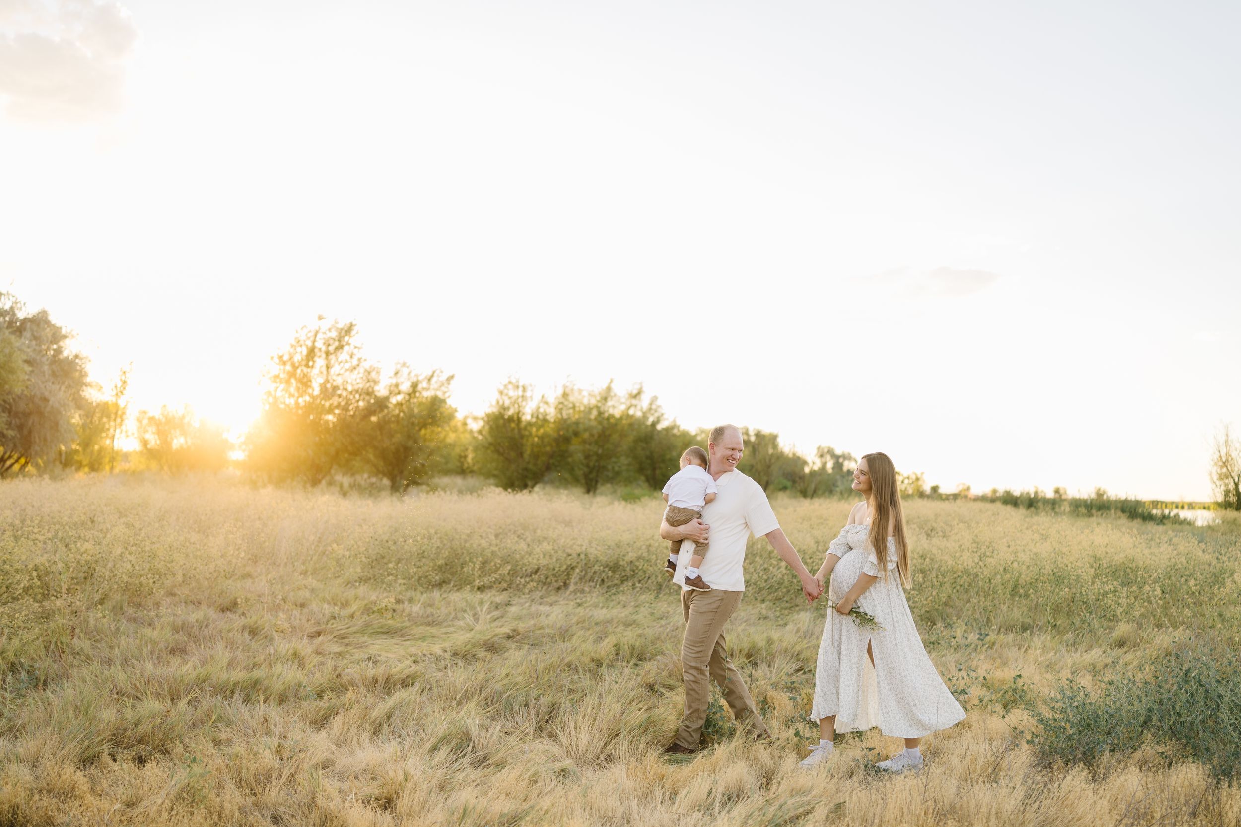 Couple in wedding attire walking through a golden field at sunset.