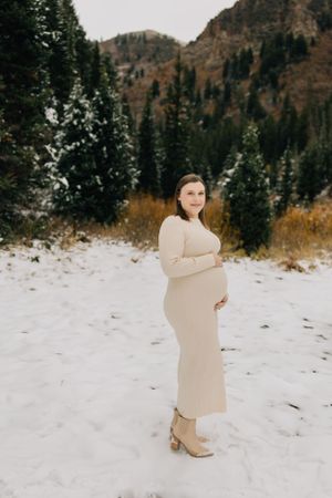 Person in a beige dress standing in a snowy mountain landscape.