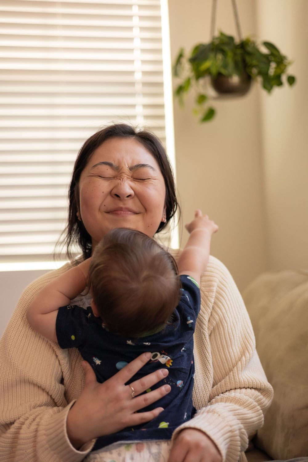 Toddler boy grasping for mom's hair and neck, while mom closes her eyes tightly while holding him in a special moment in this in-home sessio