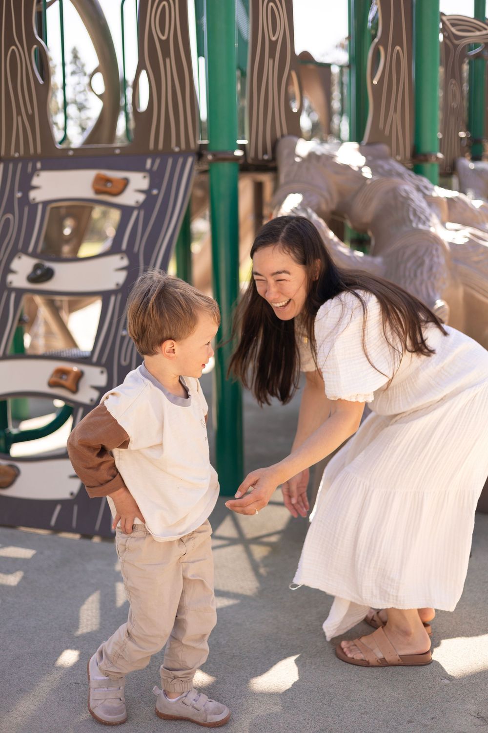 Spontaneous moment of little boy walking away from the mom, who has a huge smile trying to tickle him in a playground in San Diego.