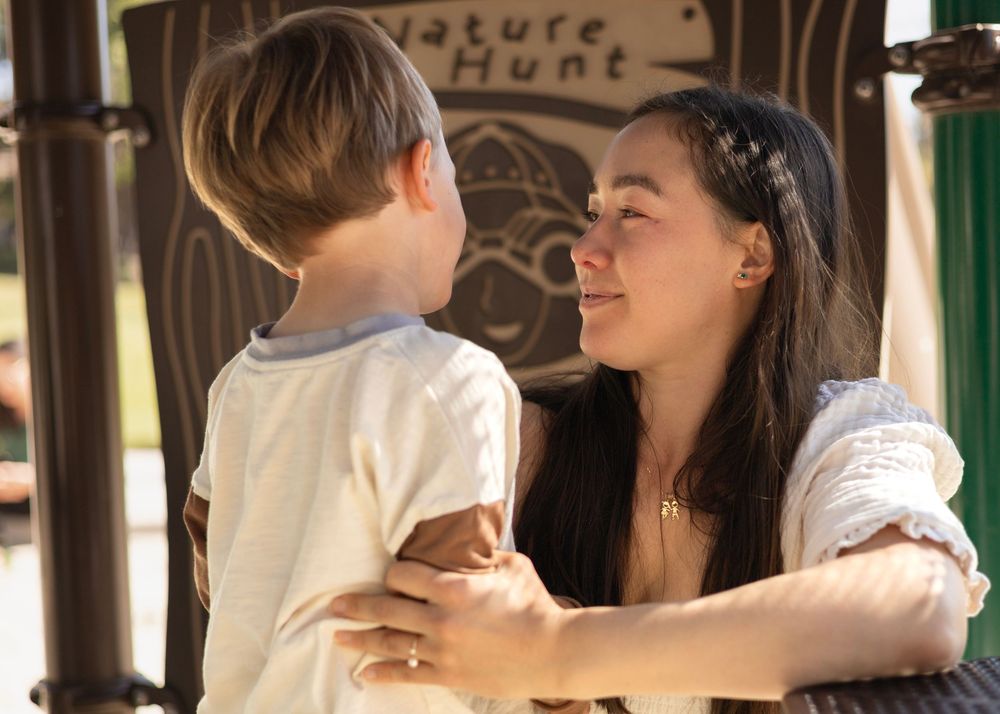 Mom looking with warm eyes at her son, who is telling her something at the playground in an intimate bond in San Diego.