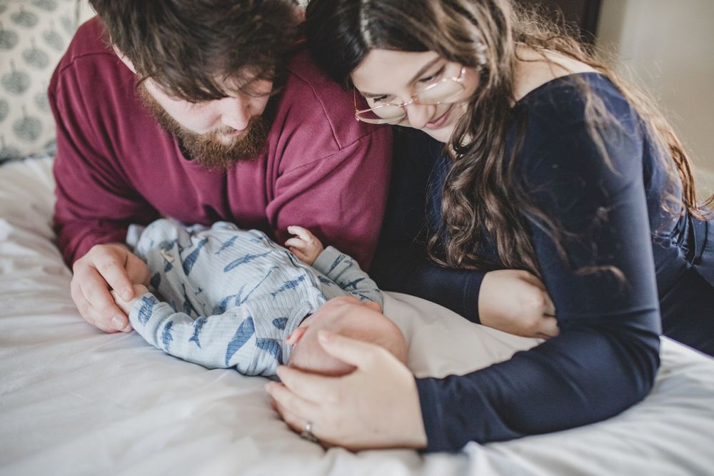 Two people lying on a bed tenderly bonding with a newborn baby wrapped in blue swaddling cloth.