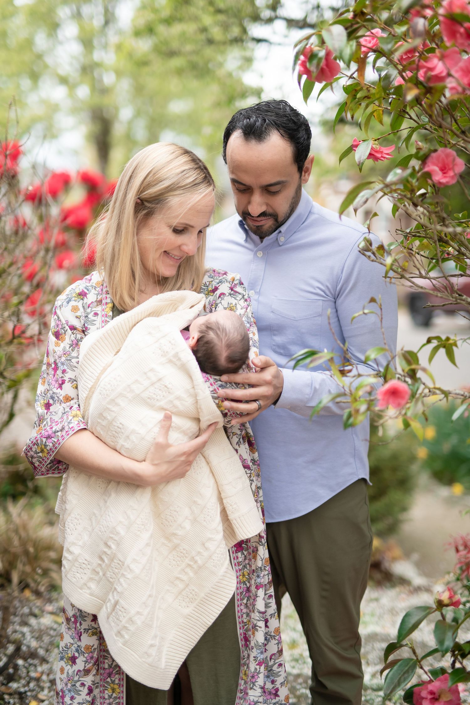 Family with baby in floral garden setting surrounded by pink blooms.