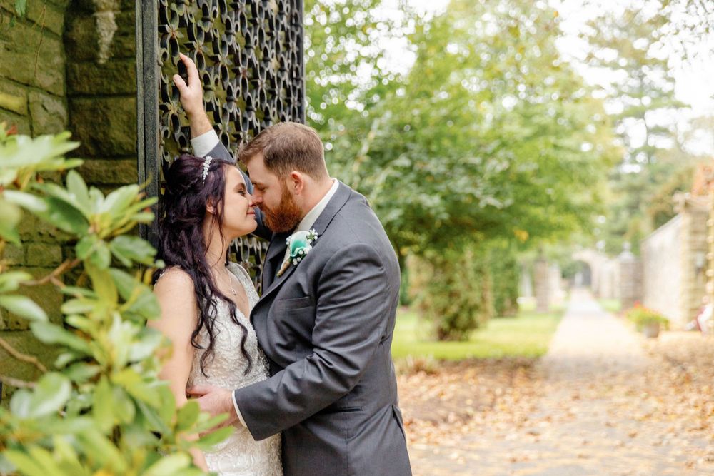 A tender moment between newlyweds sharing their first kiss as a couple next to an ivy-covered stone wall.
