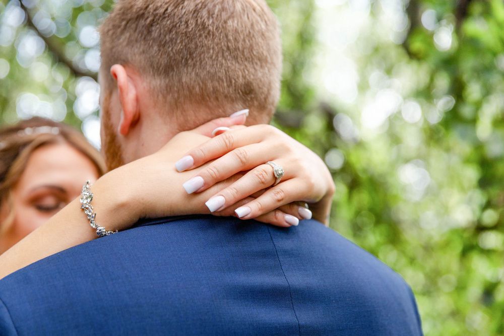 Close up view of embracing couple with hands showing white manicured nails against navy suit in outdoor setting.