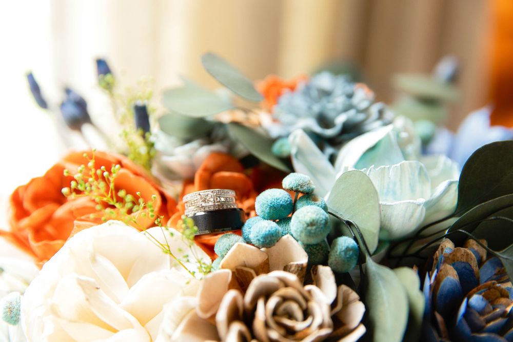 Close-up view of an artificial floral arrangement with orange roses, brown petals, and blue-tinted succulents.