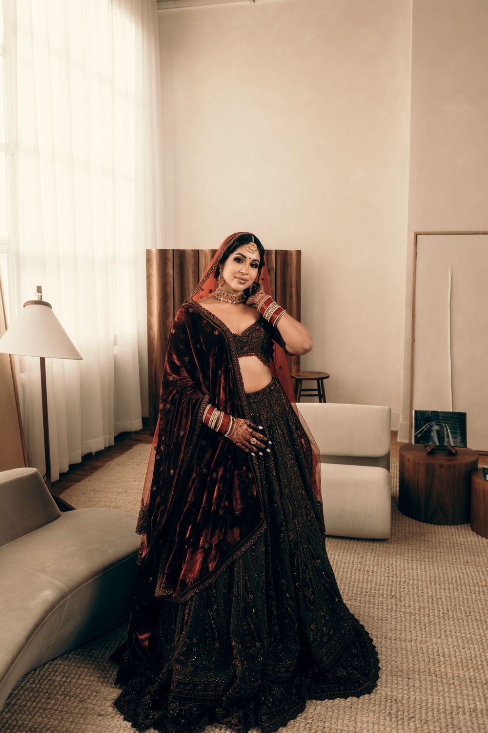Traditional Indian bridal fashion featuring an elegant black and burgundy velvet lehenga in a modern hotel room.
