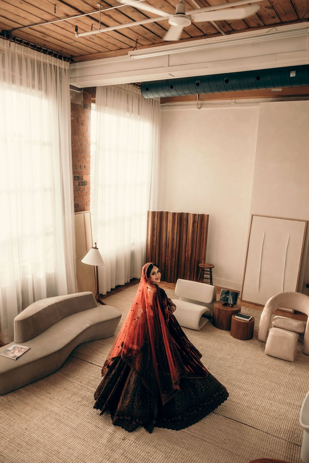 A dramatic black and red ballgown stands out against white curtains in an industrial-style room with curved seating.