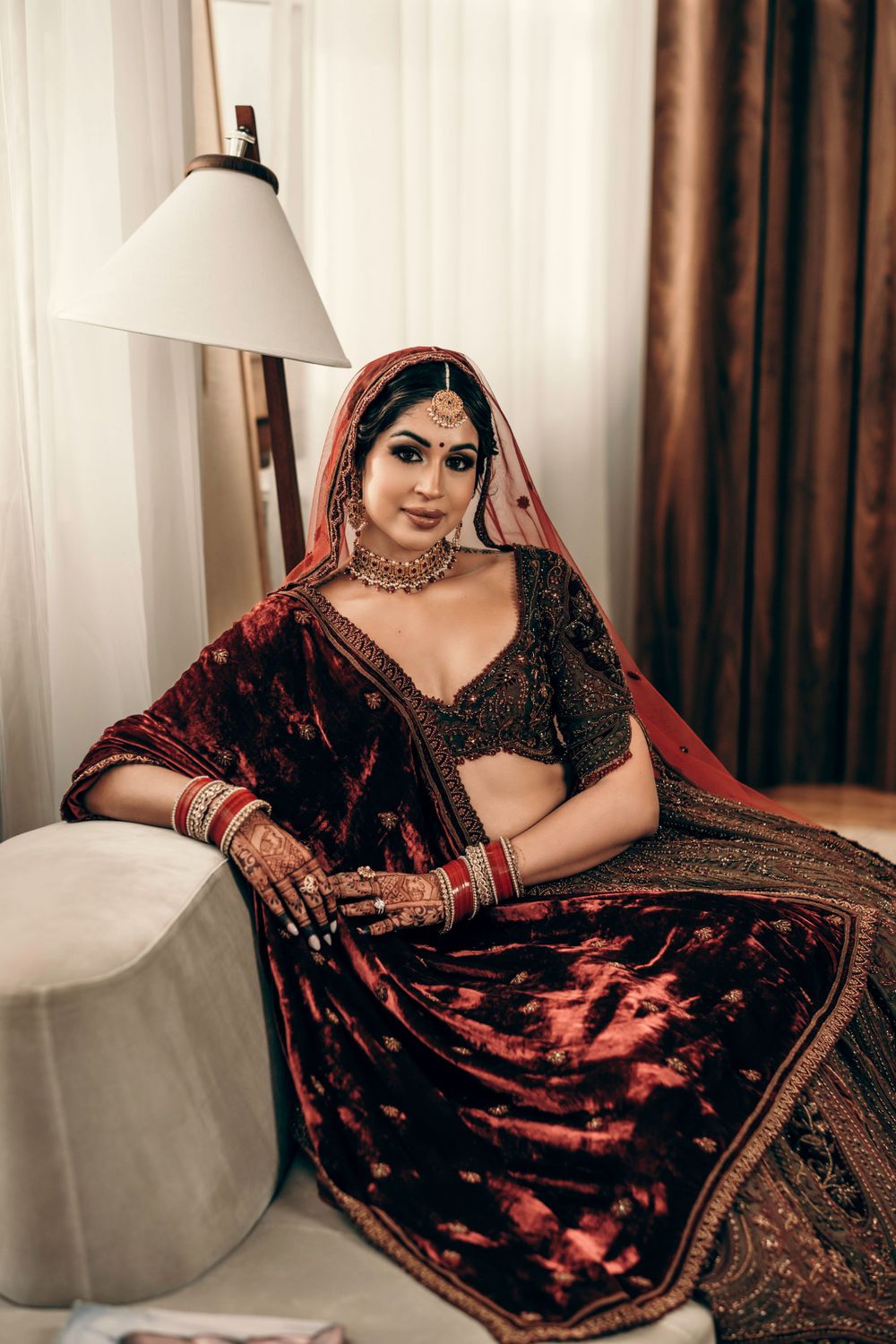 A traditional Indian bridal portrait featuring an embellished red and black lehenga and jewelry.