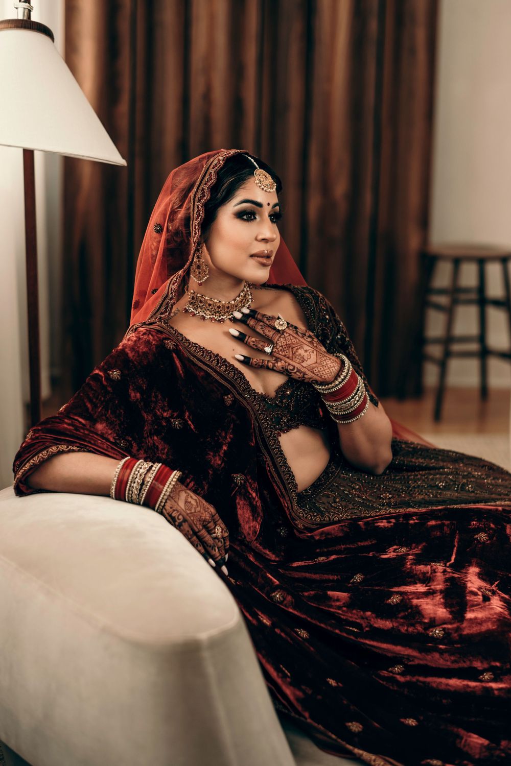Detailed view of traditional Indian bridal attire with intricate henna designs and luxurious red and black velvet clothing.