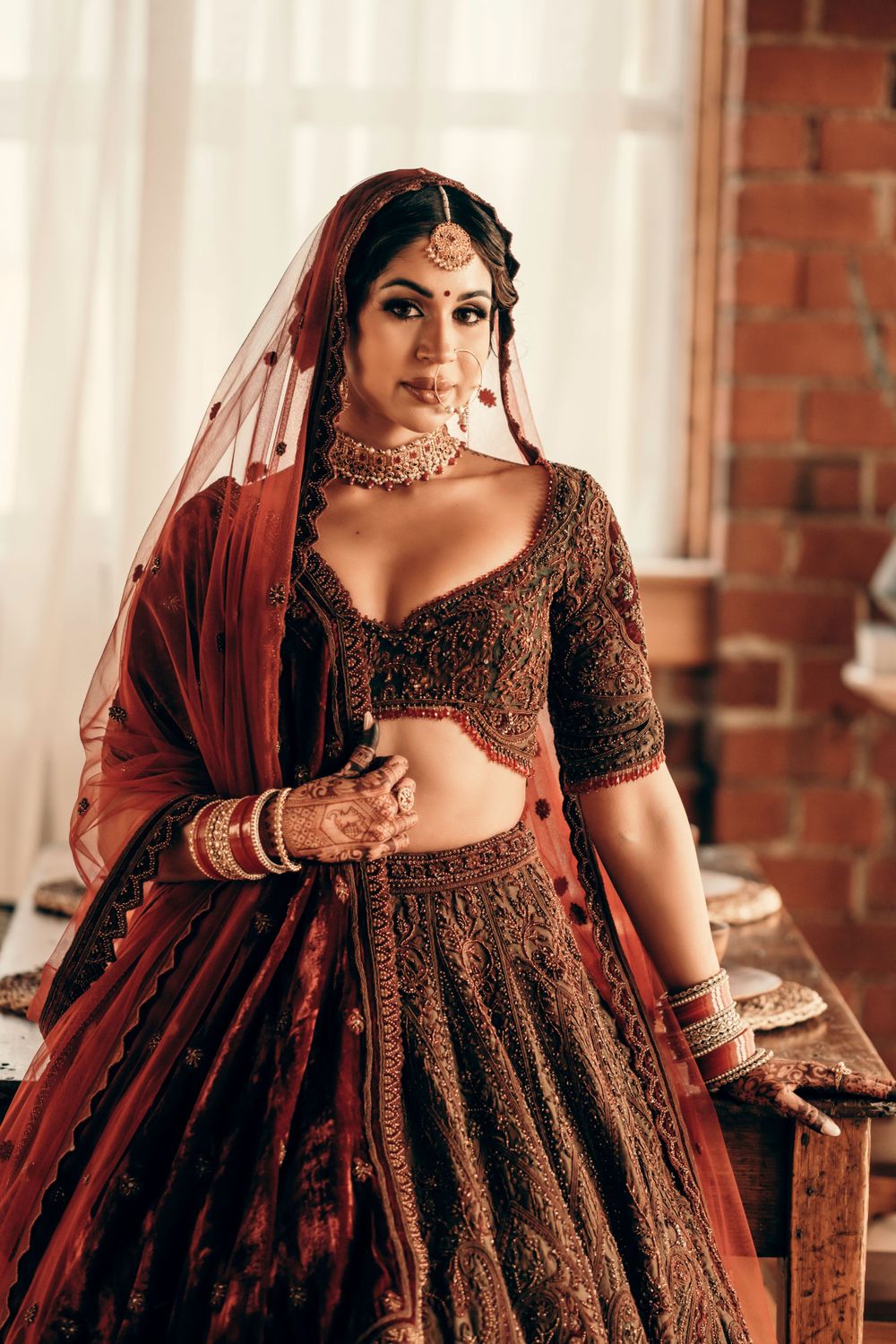 A detailed shot of traditional Indian bridal attire with burgundy lehenga, jewelry and intricate embroidery.
