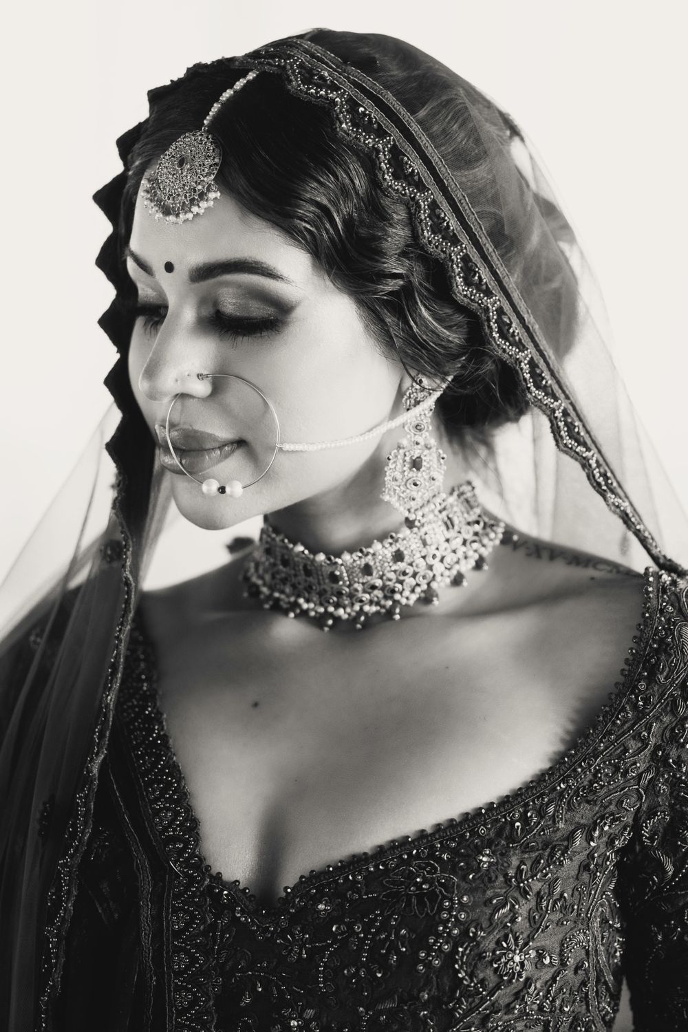 Black and white portrait of a bride in traditional South Asian wedding attire with ornate jewelry and embroidered veil.