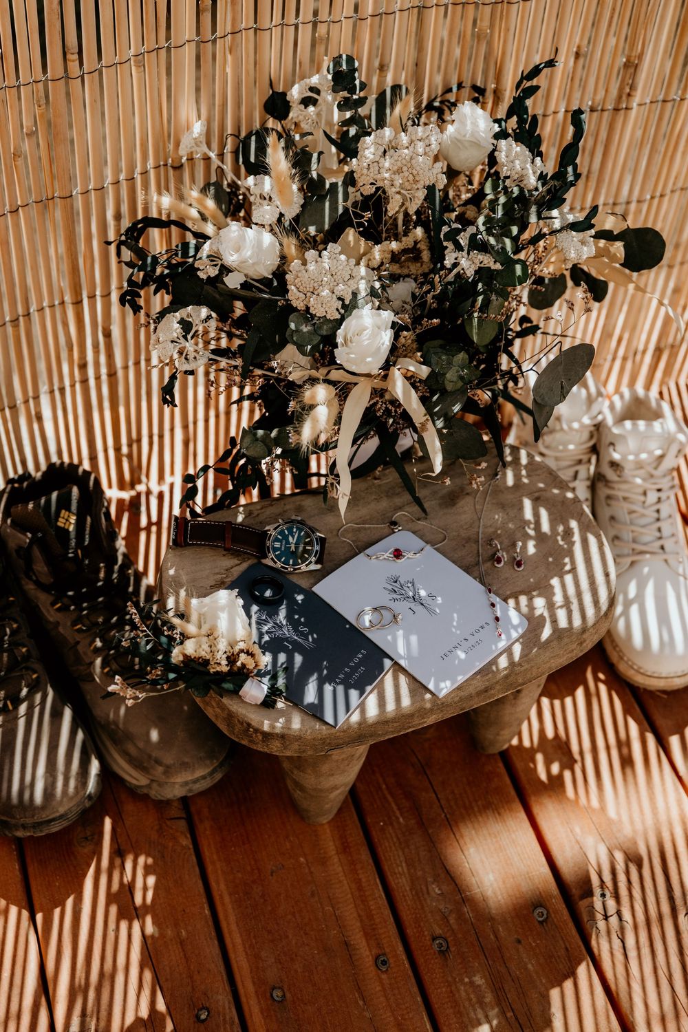 White floral arrangements on wooden surface with bamboo backdrop creating shadow patterns.