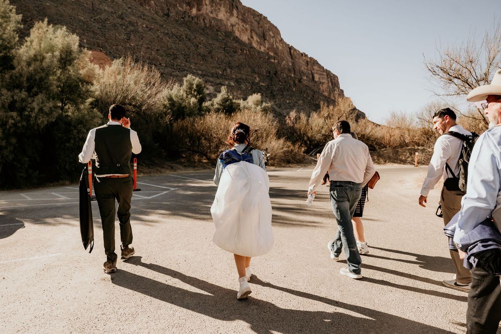 Wedding party walks along a scenic desert trail with towering canyon walls in the background.
