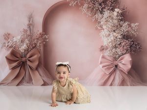 A baby with a pink bow headband crawls and poses for milestone photos on a pink floral backdrop with gold accents.