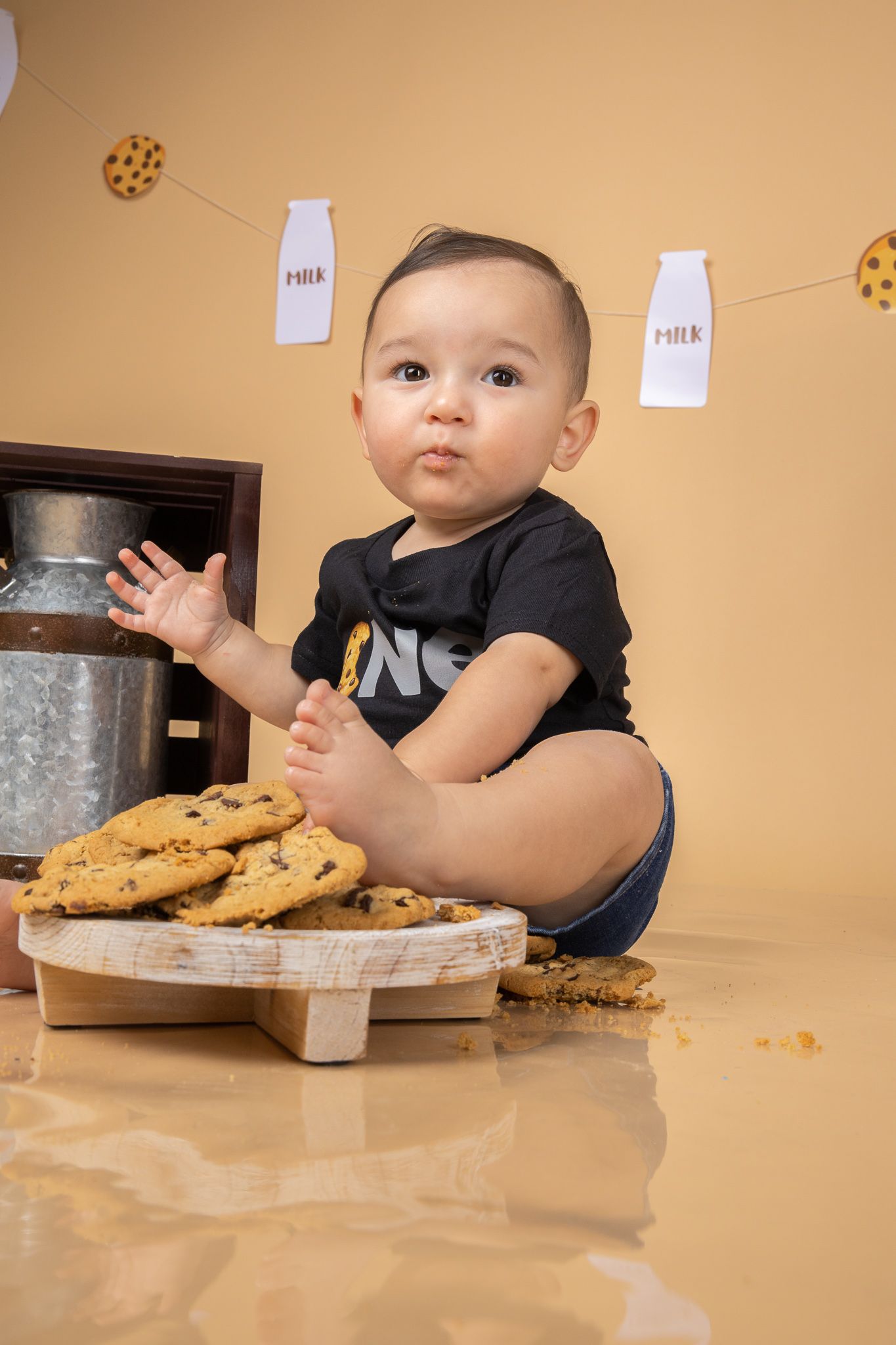 Baby sitting with plate of chocolate chip cookies against orange background.