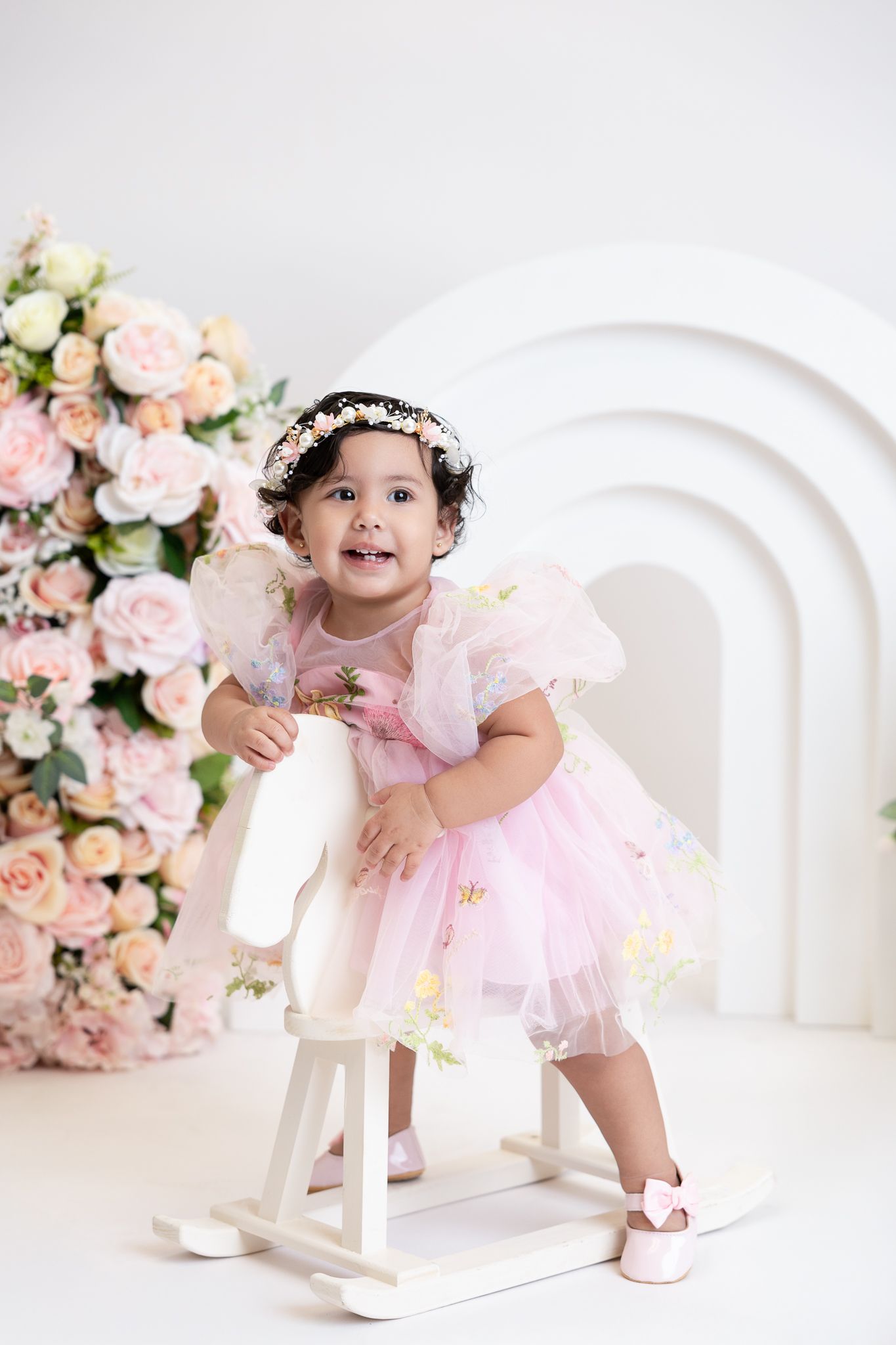 Sweet pink ballet-themed photo setup with white rocking horse and delicate floral arrangements against clean white backdrop.