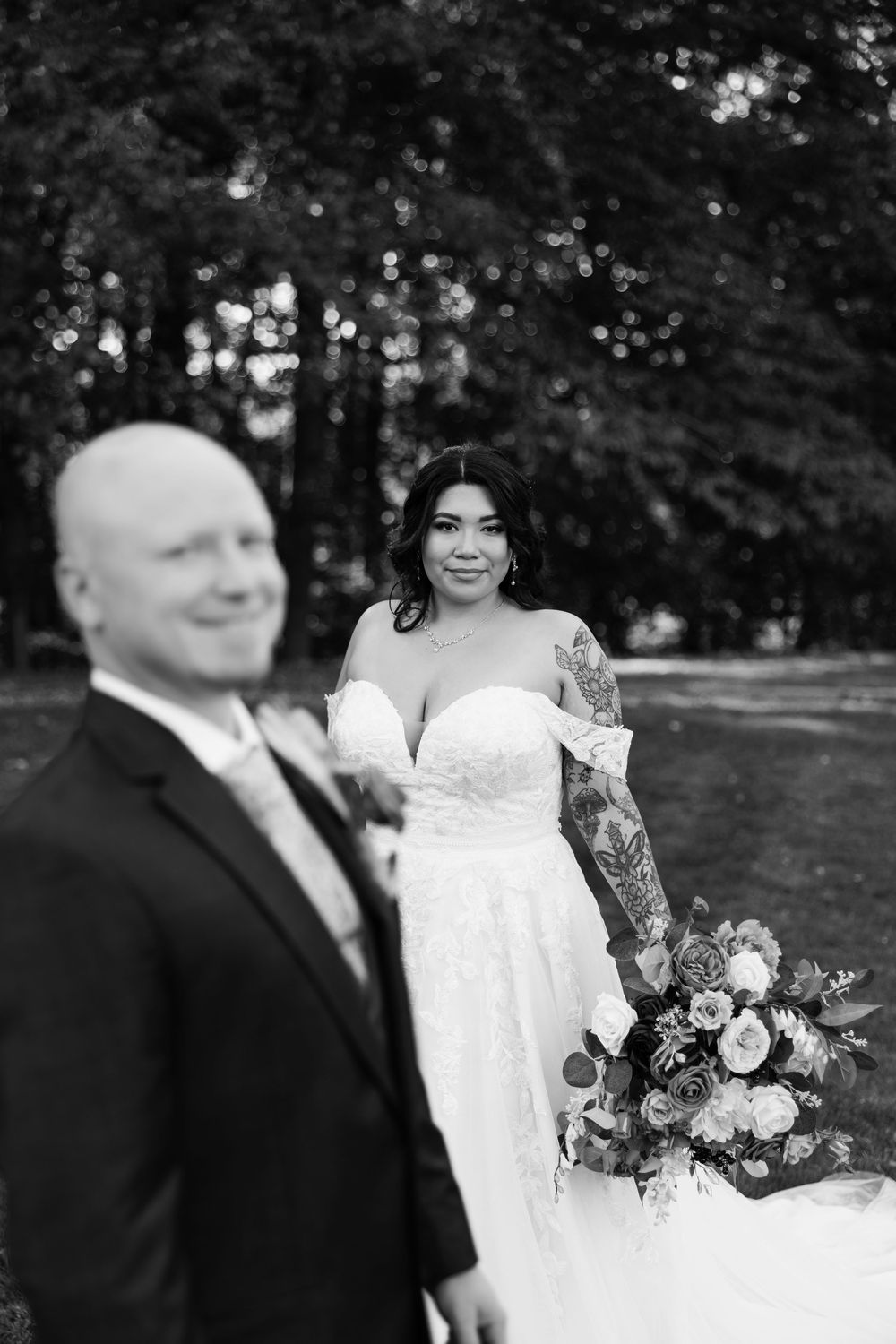 A bride and groom share a candid moment outdoors with a beautiful floral bouquet.