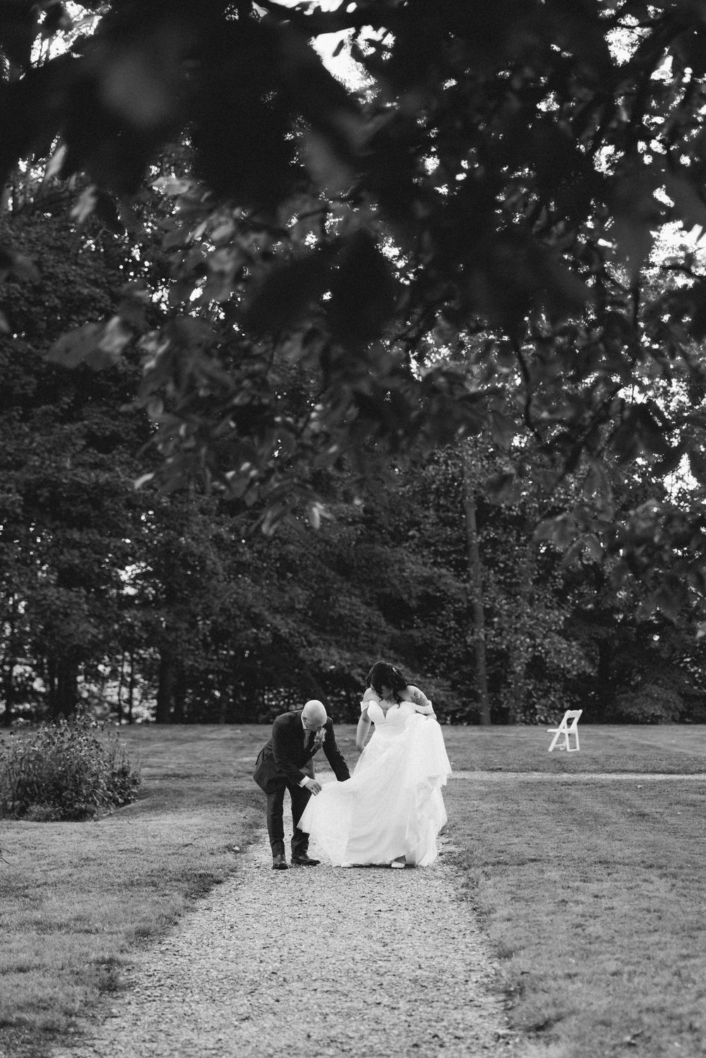 A black and white photograph shows a couple walking down a garden path during a wedding celebration.