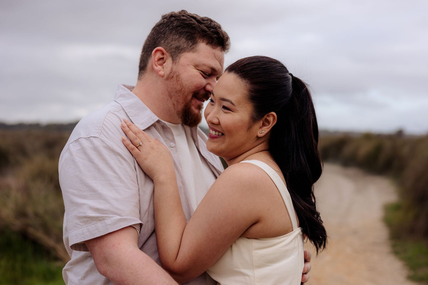 A couple shares romantic moments together on a sandy beach path during an engagement photo session.