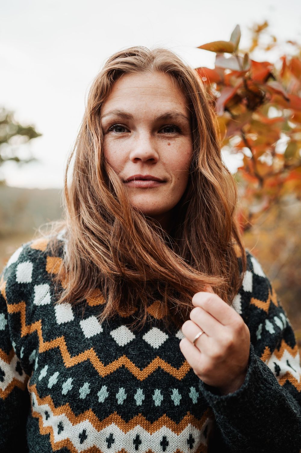 Person wearing cozy knit sweater with geometric pattern smiles against autumn foliage background.