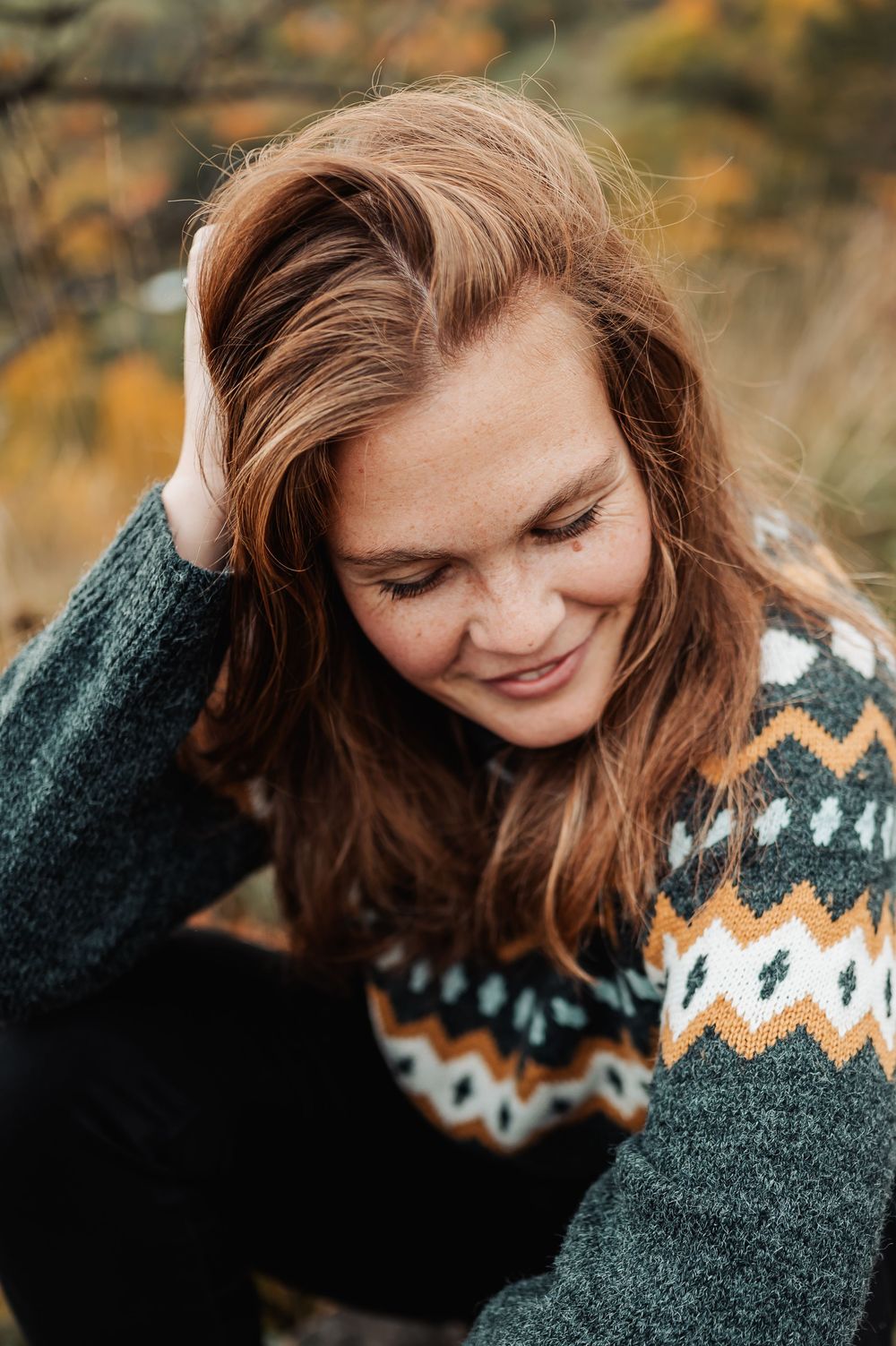 A candid autumn portrait featuring a cozy Fair Isle sweater in green and white with warm fall colors in the background.